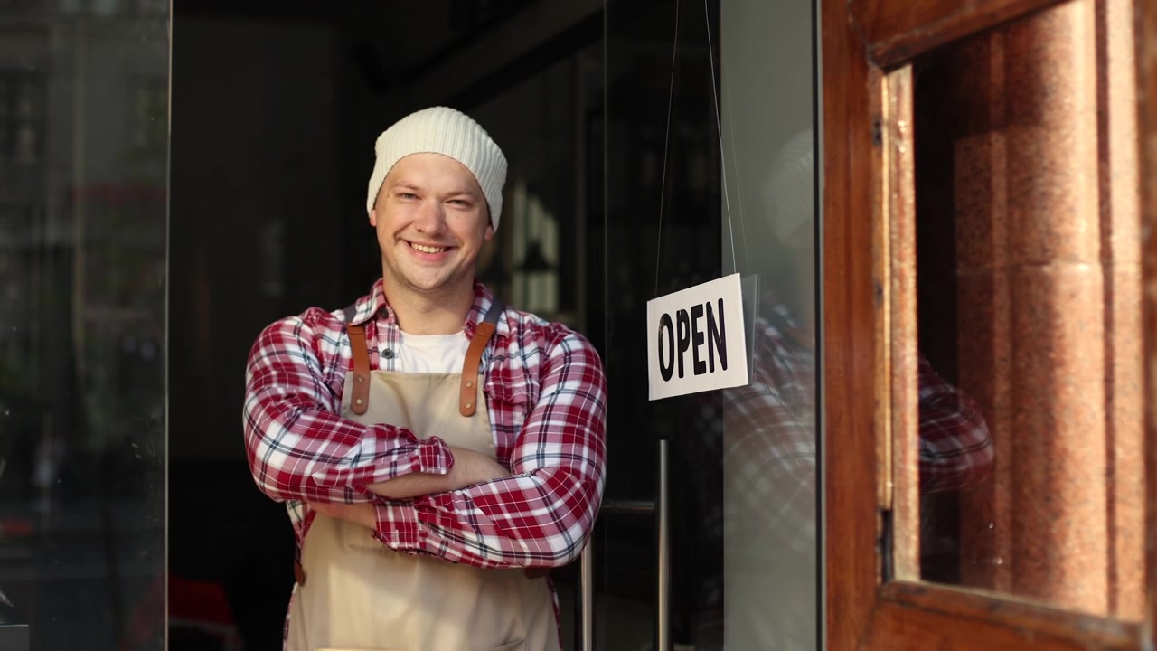Uomo sorridente gira l'insegna da Chiuso ad Aperto all'ingresso del negozio
