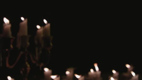 a group of white candles some on a candelabra lit up out of focus and pulled into focus and running for a while