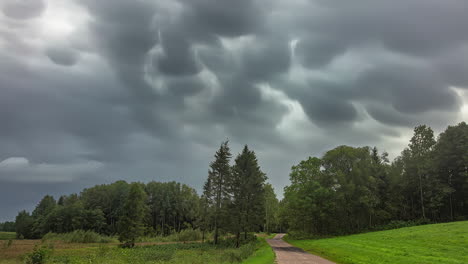 time lapse of dark rainy clouds moving above green forest and countryside road