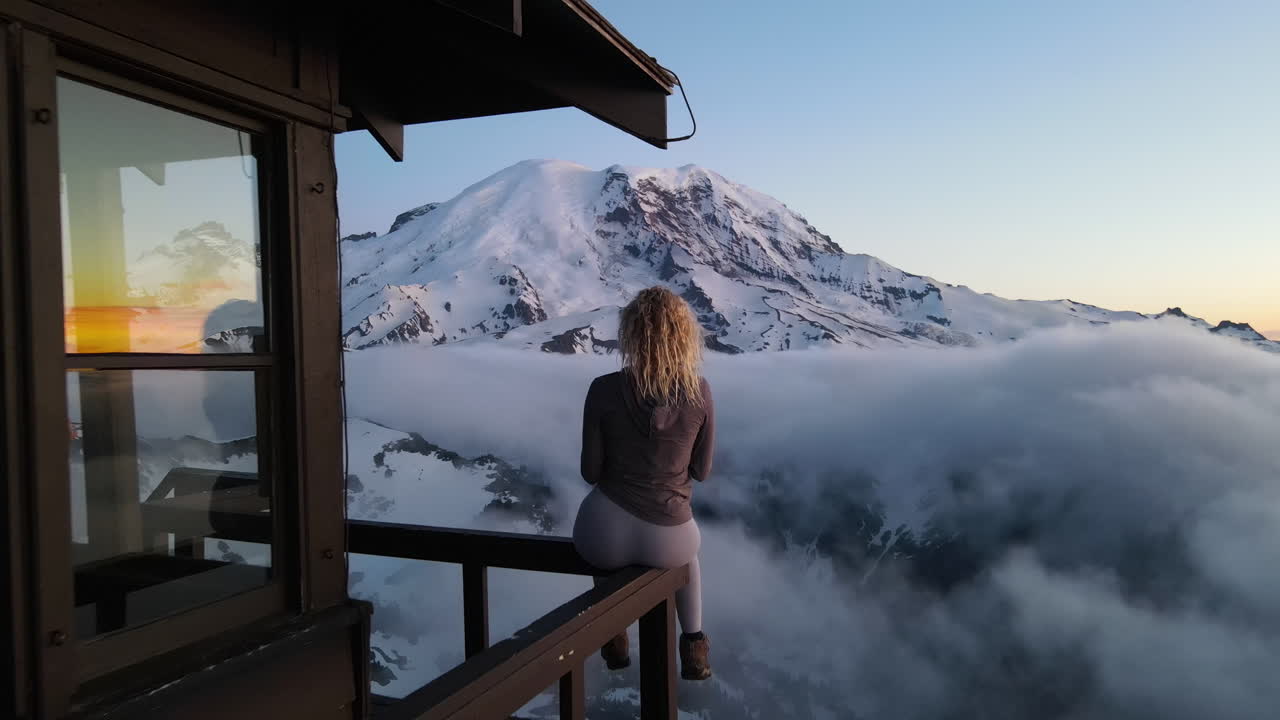 Beautiful blonde girl standing on the Mount Fremont Fire Lookout and watching Mount Rainier at sunset