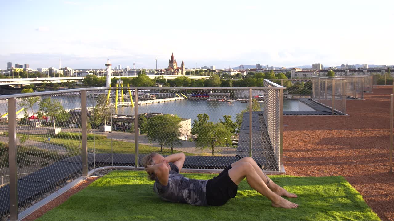 entusiasta del fitness está haciendo abdominales en una terraza de lujo con barcos en el río danubio en la parte de atrás en viena, austria, 4k