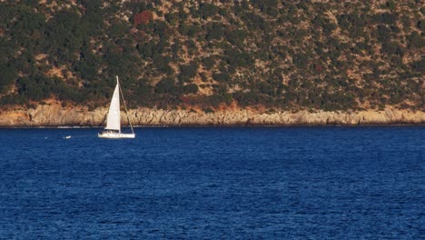 white sailboat on blue ocean beach in kefalonia, greece - wide shot