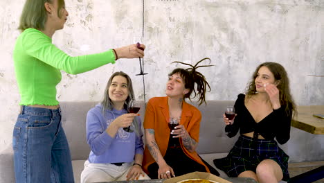 group of four female friends toasting with red wine and sharing pizza while having a fun party at home