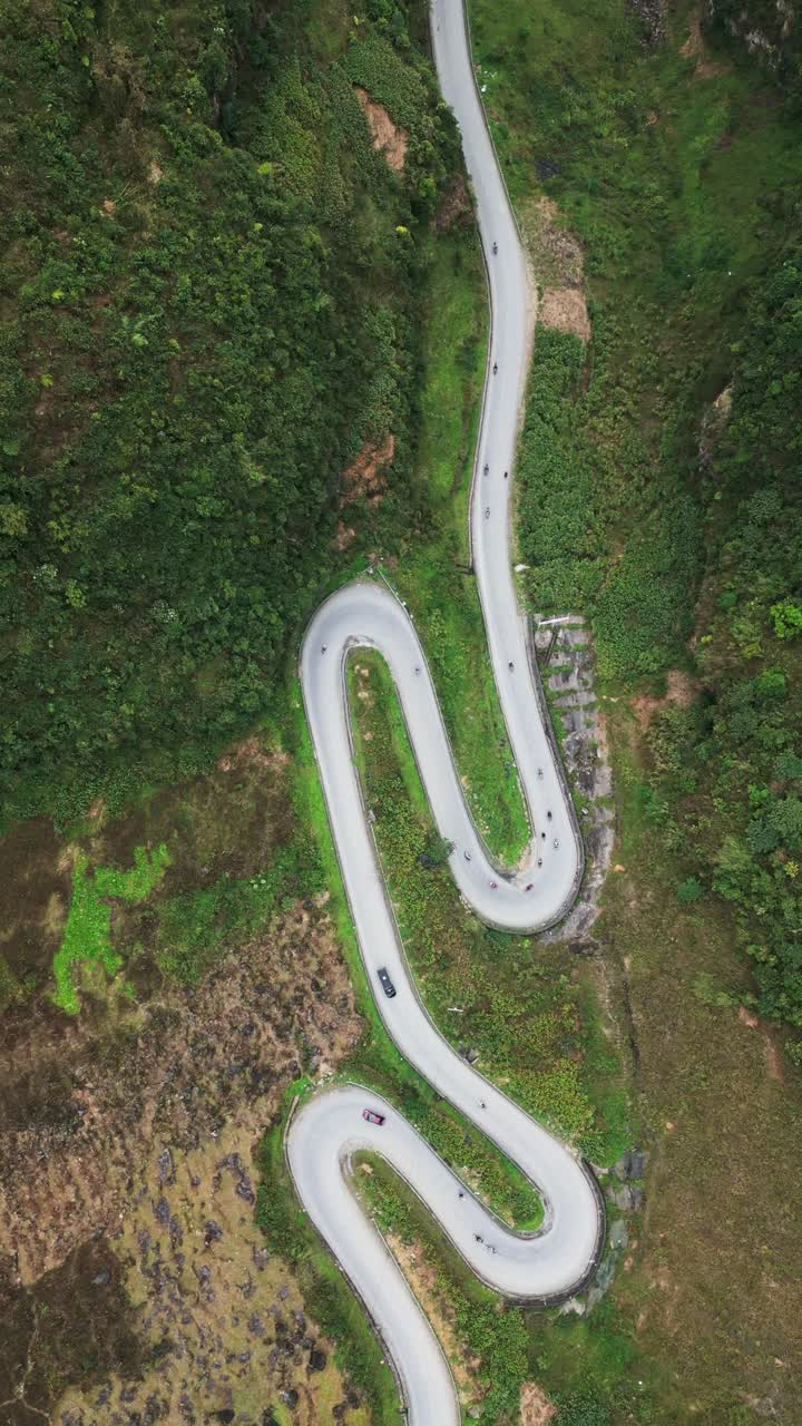 Vertikalt dronebilde ovenfra av en svingete fjellvei langs en grønn dalside med motorsykler som kjører gjennom ulendt terreng i Nord-Vietnam.