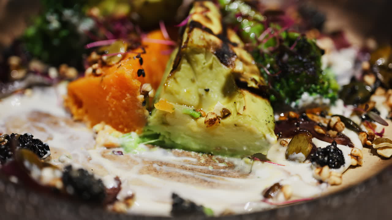 Close up of a woman eating salad with grilled avocado, sweet potato and broccoli on a plate at a restaurant