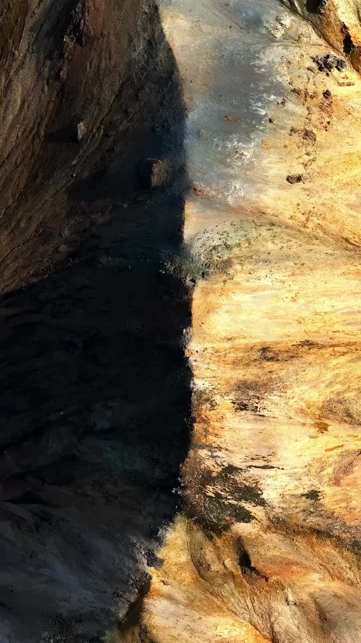 A top-down aerial view reveals a near-perfect split of dark volcanic rock and bright mineral earth, creating a dramatic symmetrical contrast shaped by Iceland’s rugged geothermal landscape