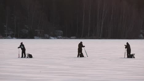 Fishermen on frozen lake drill holes in the ice, static slow motion