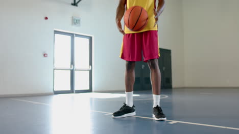 young african american man holds a basketball in a gym