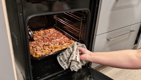 Man-Opens-Oven-Door-in-the-Kitchen,-Takes-Out-Cooked-Food-and-Places-it-on-the-Counter