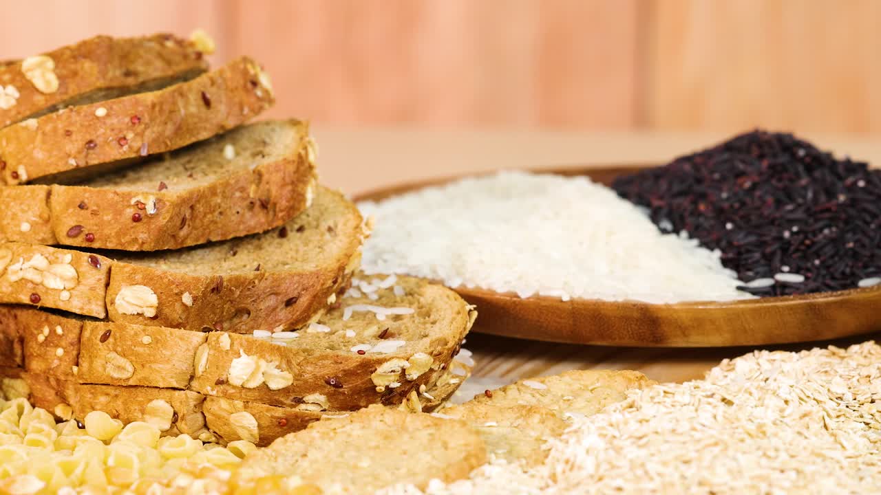 Whole wheat bread and various grains arranged on a wooden table with warm lighting