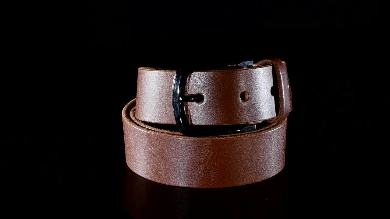 갈색 남성의 벨트는 검은색 배경에 회전합니다.