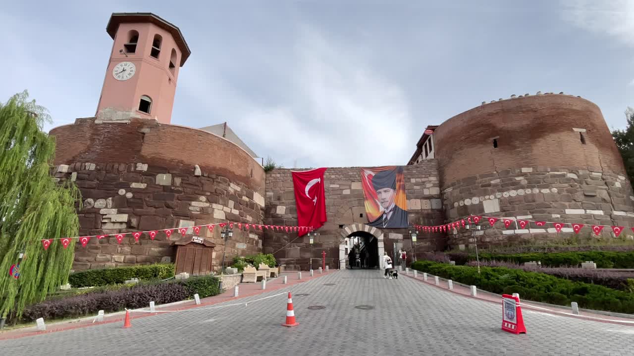 Turkey,Ankara,Ankara Castle decorated with one huge Turkish Flag on the left and a flag with Ataturk's photo on the right side of the entrance, white clouds with blue skies.People walking around.