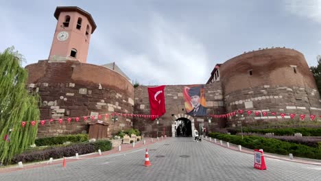 turkey,ankara,ankara castle decorated with one huge turkish flag on the left and a flag with ataturk's photo on the right side of the entrance, white clouds with blue skies.people walking around.
