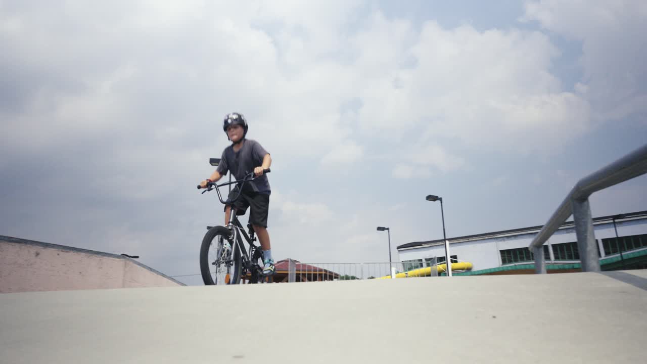 Un ragazzo con il casco va in bicicletta BMX in uno skate park e tenta di sollevare la ruota anteriore.