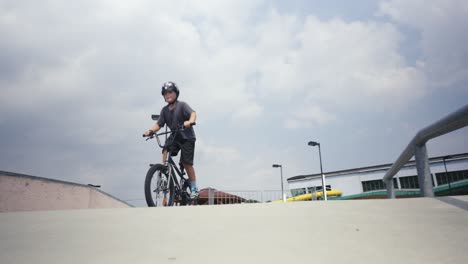 a boy in a helmet rides a bmx bike in a skate park and tries to lift the front wheel