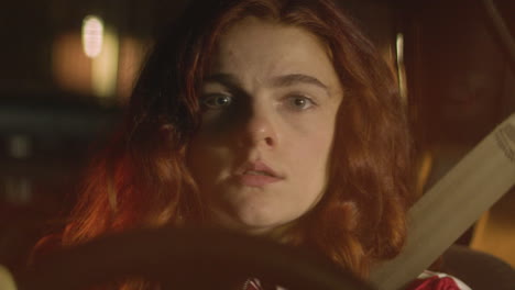 a red-haired woman stares into the camera while sitting in her car