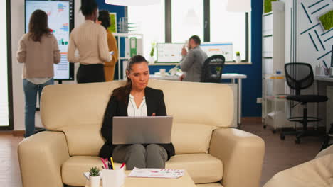 manager woman holding laptop, looking on internet while sitting on couch smiling