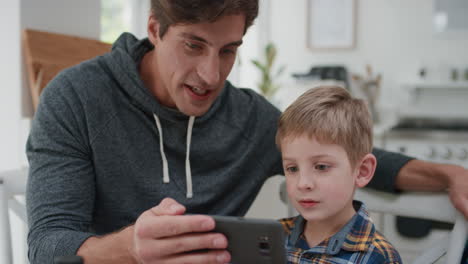 Vater-Und-Sohn-Schauen-Sich-Mit-Dem-Smartphone-Online-Unterhaltung-Auf-Dem-Handy-An.-Fröhlicher-Kleiner-Junge,-Der-Sich-Zu-Hause-Mit-Seinem-Vater-Vergnügt,-4K-Videos