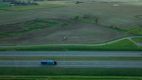 a truck driving along an empty highway flanked by open fields at sunset