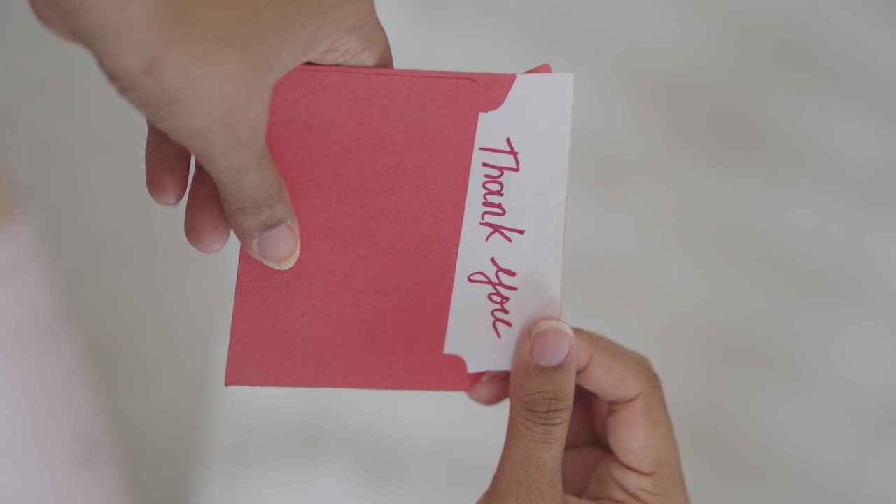 Hands placing thank you card in a red envelope