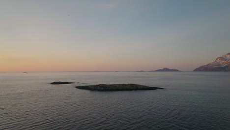 Drone-pullback-from-rocky-islands-in-ocean-at-sunset,-chased-by-Oystercatchers