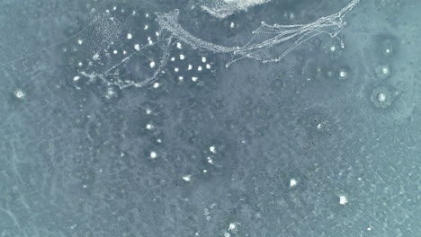 Beautiful-aerial-top-down-shot-of-frozen-blue-lake-along-with-snow-covered-trees-on-the-bank-on-a-winter-landscape-at-daytime