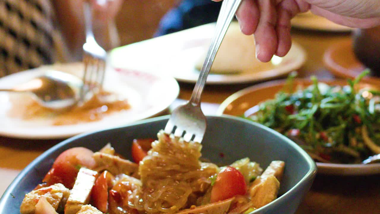 Diners enjoy spicy rice vermicelli salad with tofu and tomato in warmly lit Bangkok restaurant
