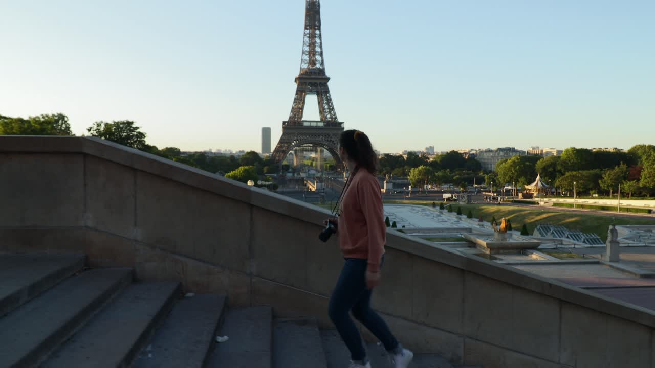 Young attractive woman walking up stairs at the trocadero with the Eiffel tower in the background during early summer morning