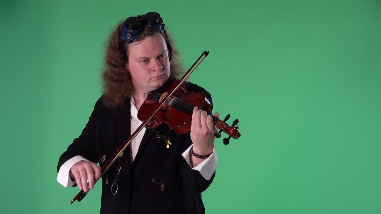 검은색 의복과 오리지널 안경을 입은 바이올리니스트는 바이올린을 마스터리하게 연주합니다. 남자는 멜로디를 만들기 위해 활으로 현을 만니다. 녹색 화면 크로마 키. 느린 모션. 클로즈업
