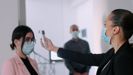 business woman with face mask checking collegues forehead temperature