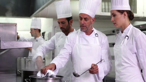 Chef-showing-colleague-content-of-pot-and-smiling-at-camera