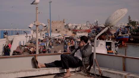 Man-speaks-on-cellphone-while-overlooking-crowd-in-port-market-of-Essaouira-City-north-of-Morocco