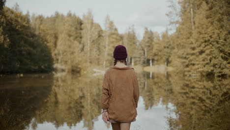 Female-explorer-walking-towards-lake-in-forest