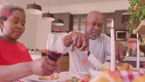 Animation-of-hearts-over-senior-african-american-couple-sitting-at-table-at-christmas