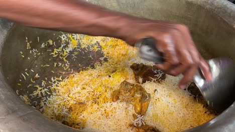 Nahaufnahme-Männlicher-Hände,-Die-Heiße,-Frisch-Gekochte-Biryani-Gerichte-Aus-Einem-Großen-Behälter-In-Einer-Küche-Verpacken