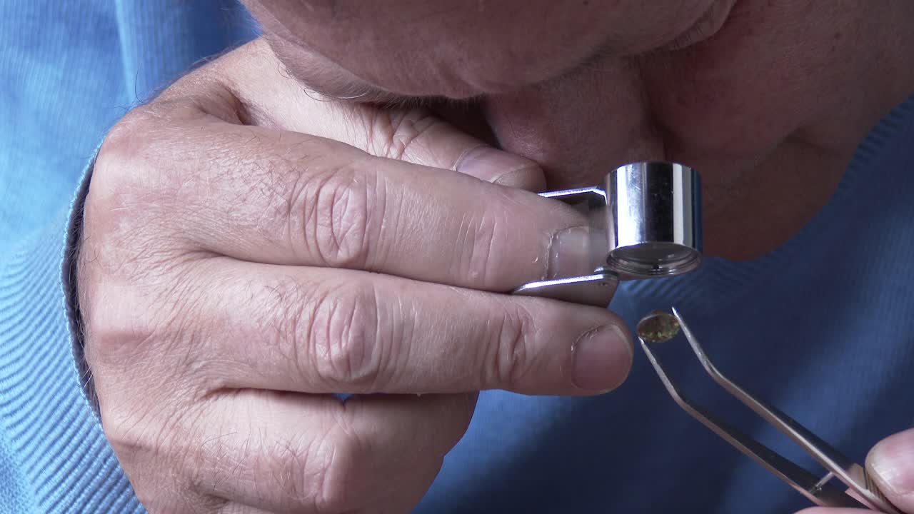 un gemólogo viendo un granate demantoide a través de una lupa de joyero, de cerca