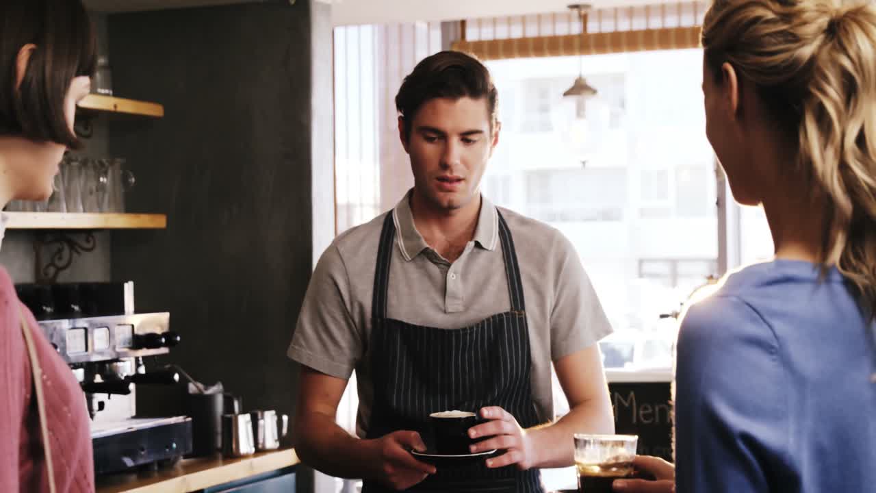 Waiter serving cup of coffee to women at counter