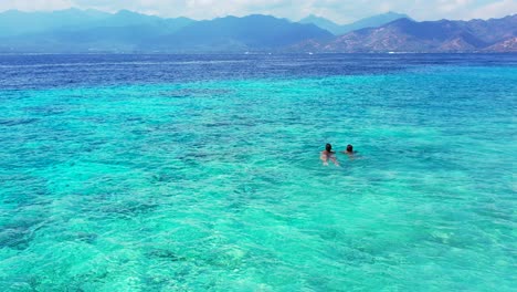 two young female teenagers swimming in the crystal clear aqua water in perfect tourist holiday destination indonesia