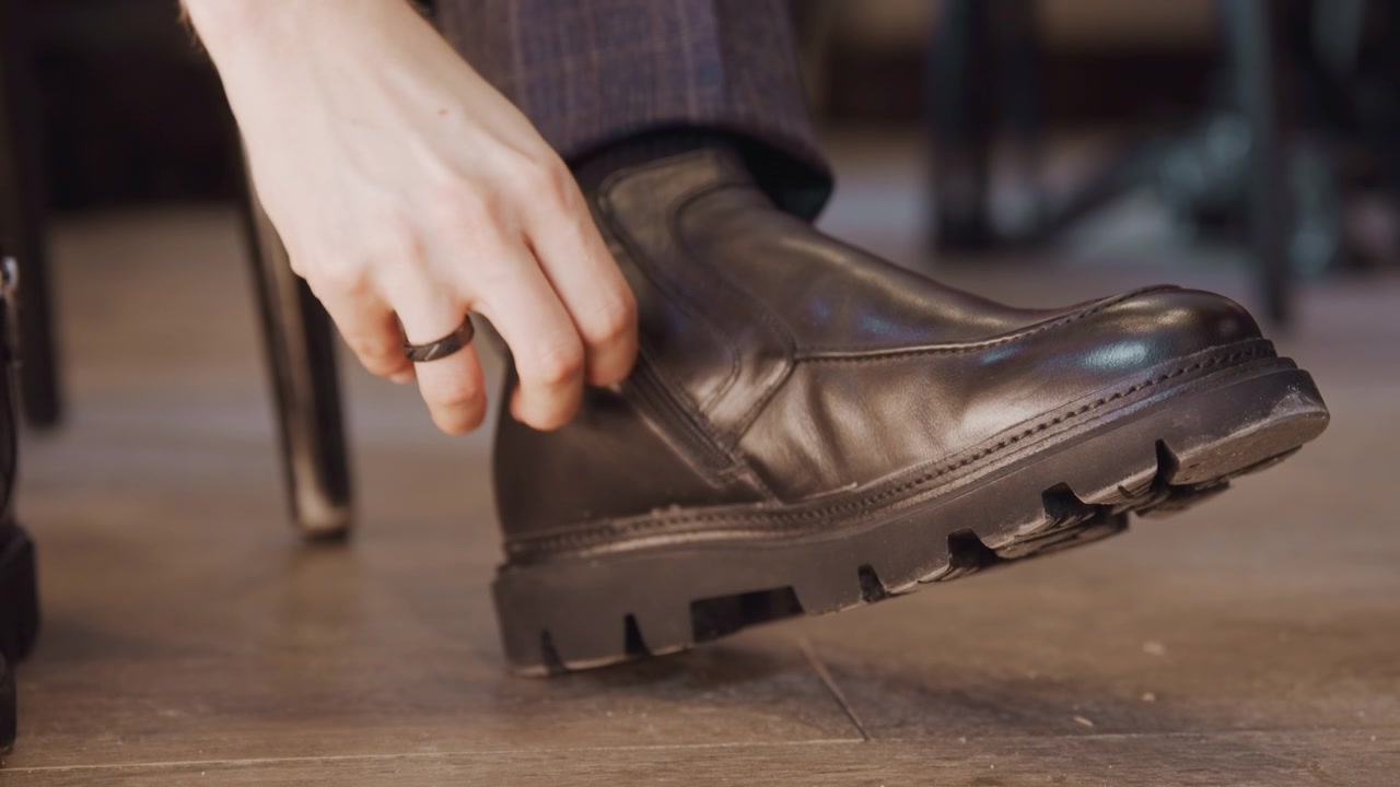 Close up of man hand adjusting zipper on his black leather boot showcasing detailed craftsmanship and texture. scene features soft lighting that highlights material quality while maintaining
