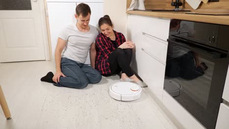 couple sits looking at robot vacuum cleaner removing trash