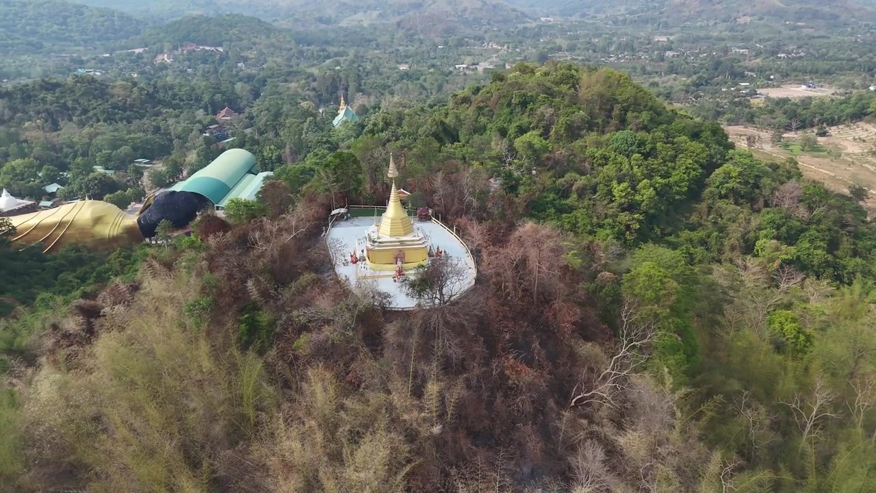 Orbita aerea attorno alla pagoda dorata che si affaccia su lussureggianti paesaggi montani rurali presso il tempio Wat Pa Sawang Bun, con un gigantesco Buddha reclinato visibile sullo sfondo, Saraburi, Thailandia.