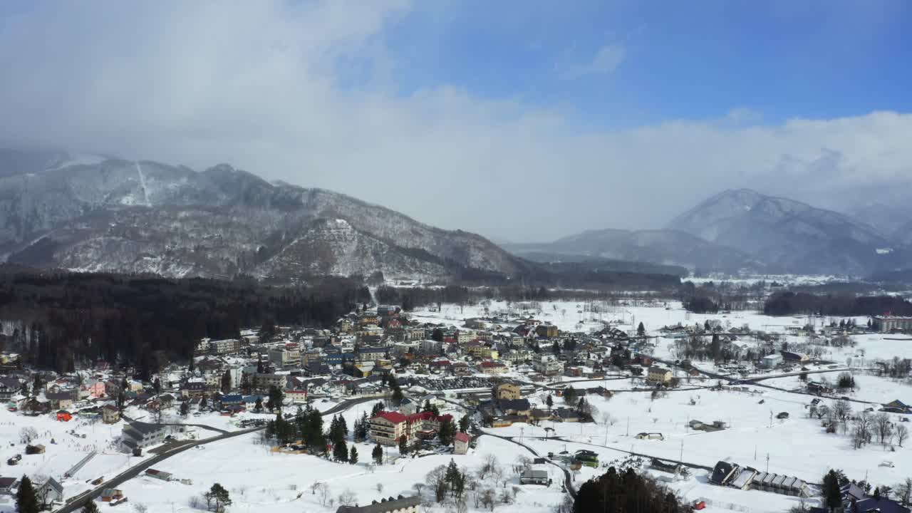The drone's perspective reveals the harmonious blend of nature and urban life, with Hakuba valley's snow-covered mountains, serene valleys, and Hakuba city's streets shining in the winter sunshine