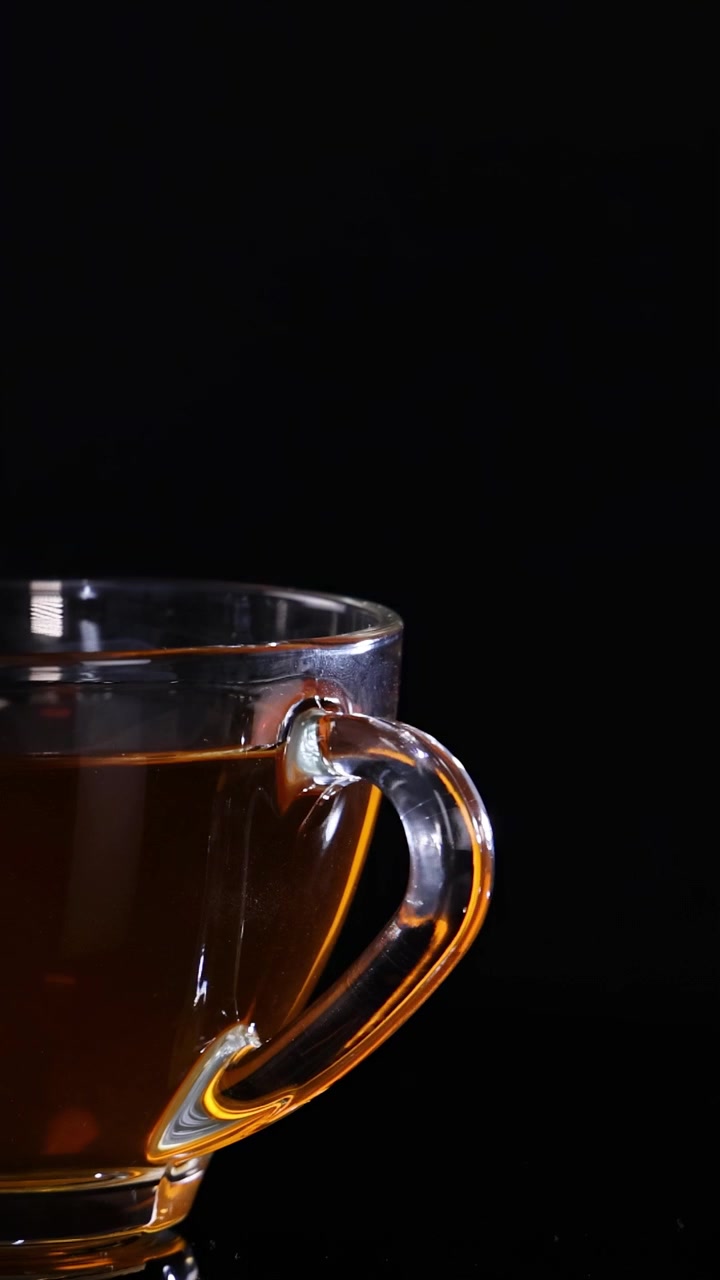 Una tazza di vetro piena di tè è ferma su uno sfondo nero, evidenziandone la trasparenza e il colore.