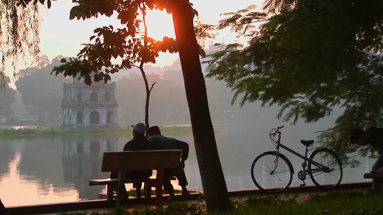 사람들은 일몰에 하노이의 공원에 앉아 경치를 감상합니다.