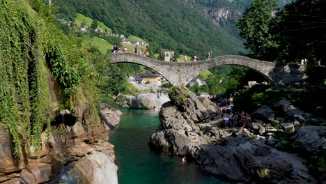 cinematic drone shot of ponte dei salti flying under the bridge and over the clear water of the verzasca river