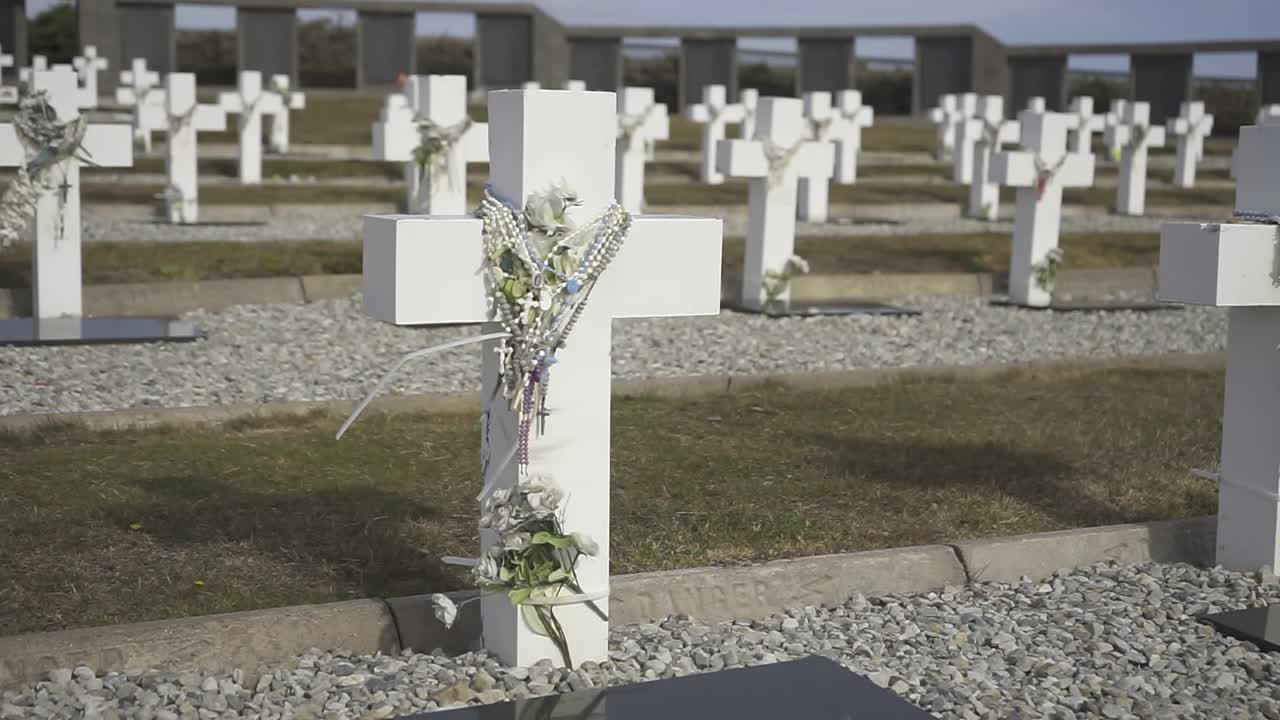 White cross adorned with flowers and ribbons stands in a vast military cemetery, a poignant symbol of remembrance and sacrifice