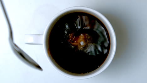 teaspoon pouring sugar into cup of coffee