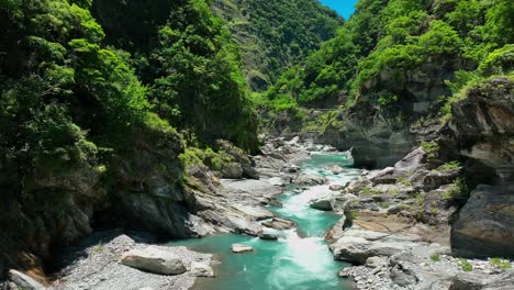 Aerial-establishing-flight-over-flowing-stream-between-rocks-surrounded-by-green-nature