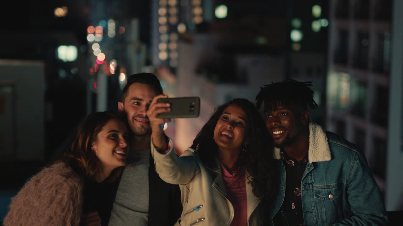 jóvenes amigos multiétnicos en la azotea por la noche posando para una foto de grupo celebrando la reunión de amistad mujer joven usando un teléfono inteligente compartiendo reunión de fin de semana en las redes sociales