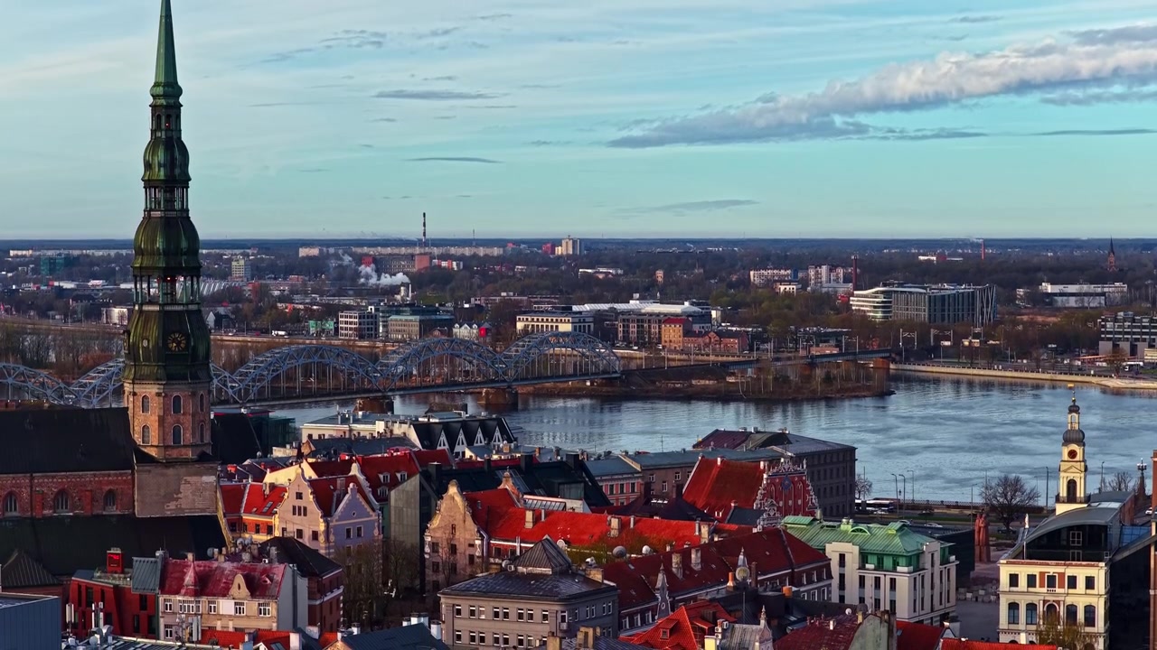Panorama aereo di Riga con la guglia della Chiesa di San Pietro e il fiume Daugava, che cattura lo skyline storico, i ponti e l'ampio paesaggio urbano della capitale della Lettonia.